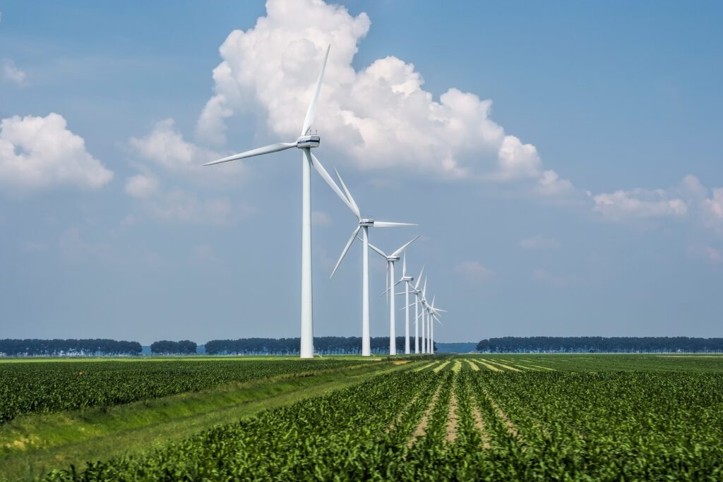 Wind turbines across Dutch farmland with green crop rows under blue sky and clouds