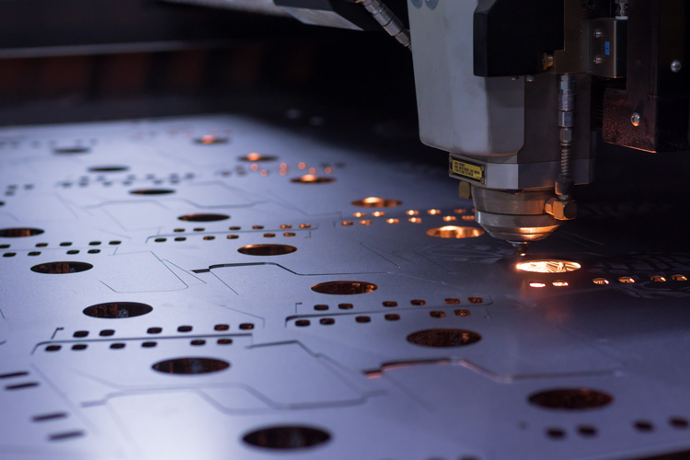 CNC laser cutter engraving perforated metal sheet with glowing sparks in manufacturing workshop.