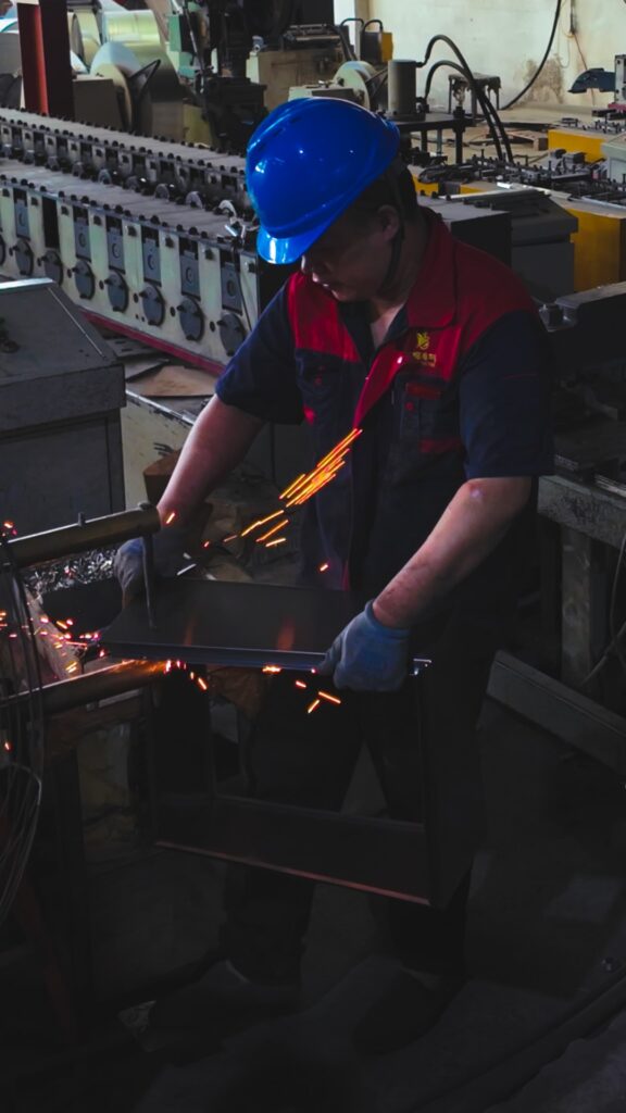 Factory worker in hard hat uses tongs to handle glowing hot metal and sparks.