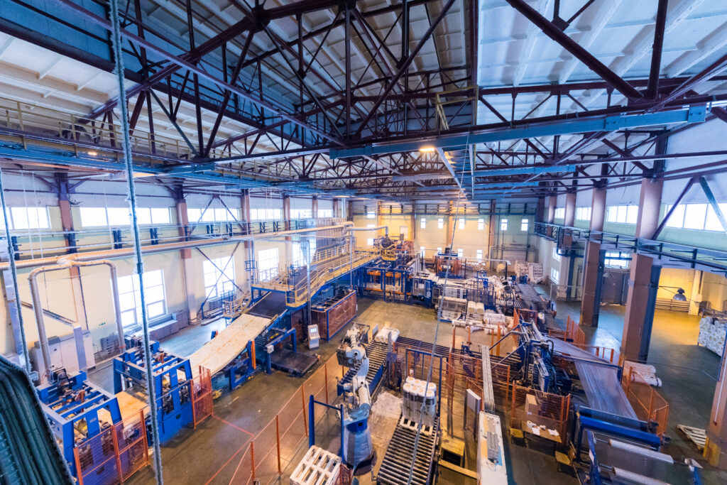 Elevated view of factory warehouse interior with machinery, pallets, and steel roof trusses