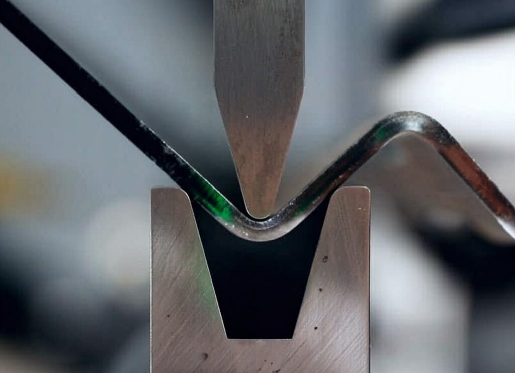 Close-up of precision metal bending using a punch and V-die on steel strip