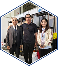 Three colleagues posing in an industrial lab workspace with equipment shelves in the background.