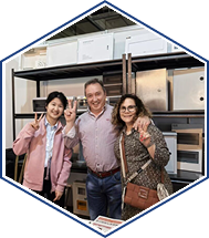 Three coworkers smiling in warehouse aisle, posing between inventory shelves with boxes