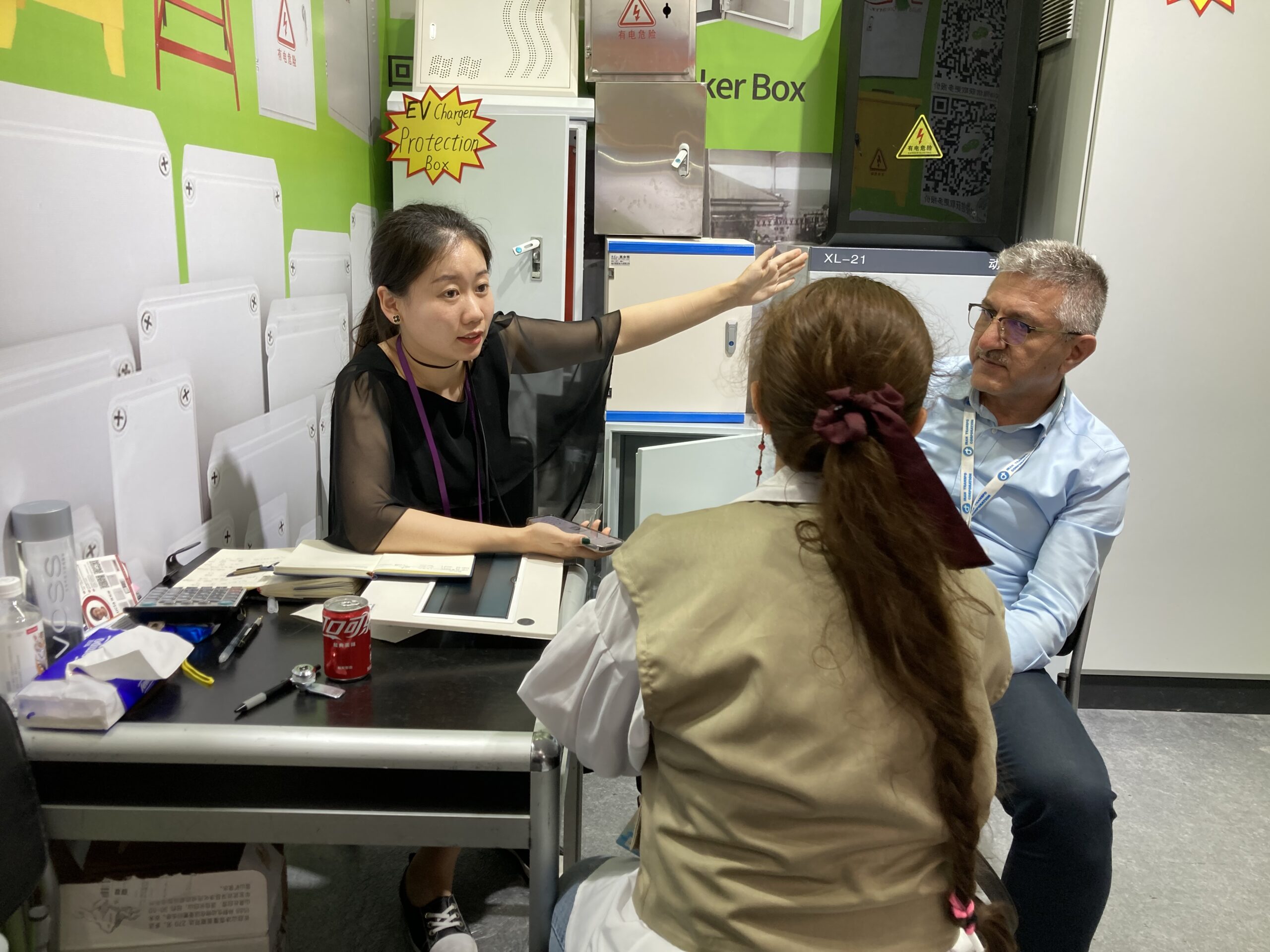Office staff member points while consulting with two visitors in a small meeting room.