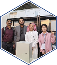 Four attendees pose at a technology exhibition booth, one flashes a peace sign.