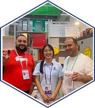 Three smiling trade show attendees with badges posing at an exhibition booth display.