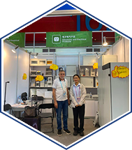 Trade show booth with green Arabic banner and two staff members welcoming visitors