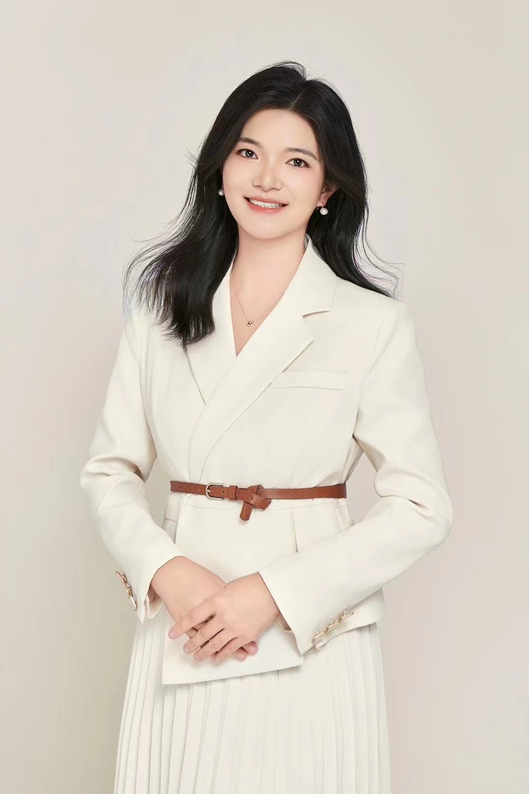 Woman in off-white blazer holding clutch, studio portrait on beige background